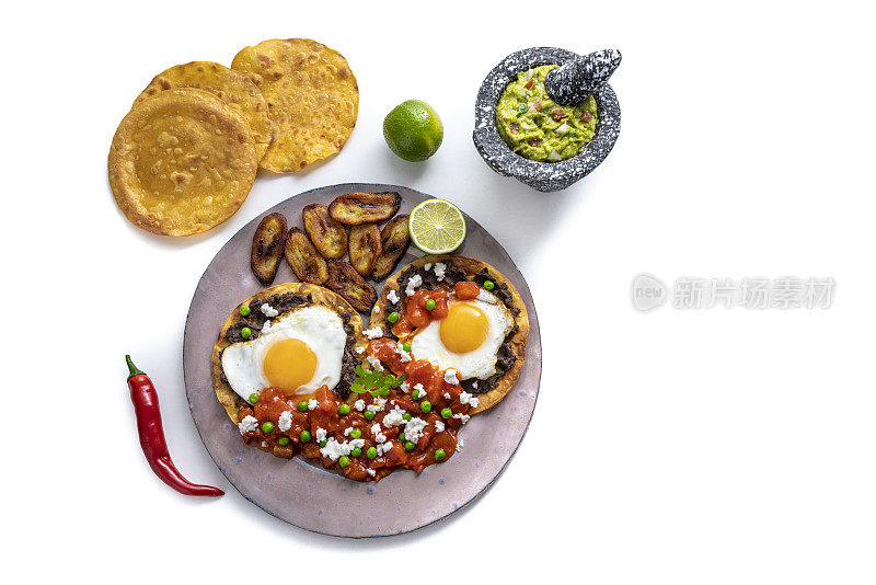 Huevos Motuleños是墨西哥moculeno鸡蛋早餐，鳄梨色拉酱孤立的白